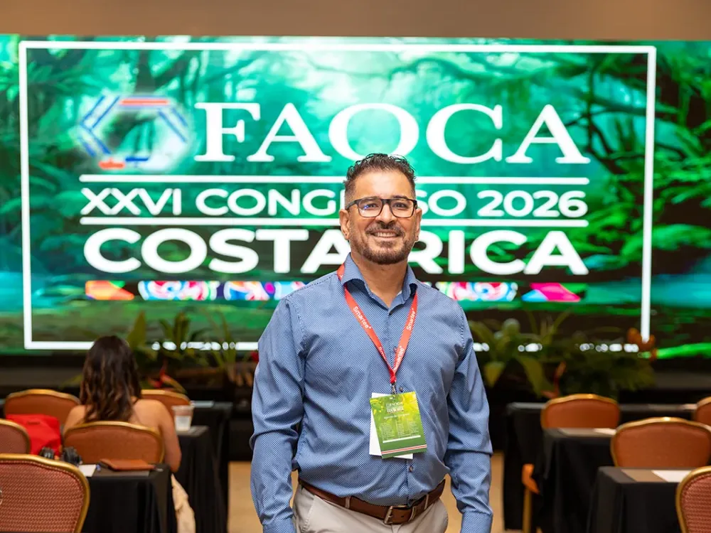 Asistente de FAOCA Costa Rica 2026 con el gafete del congreso, frente a la pantalla LED con la marca diseñada por GP Agency